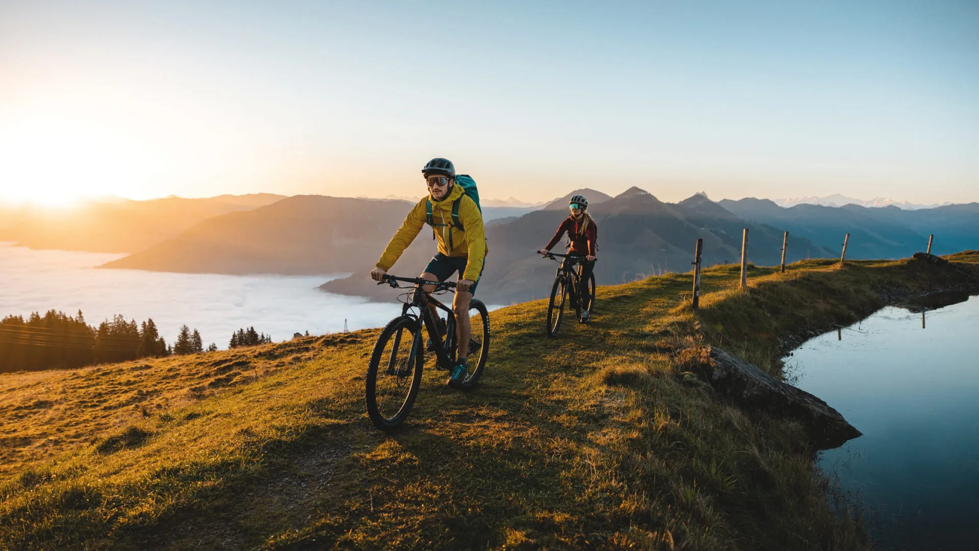 Zwei Radfahrer auf einem Pfad mit Blick auf den Brixentaler See bei Sonnenuntergang