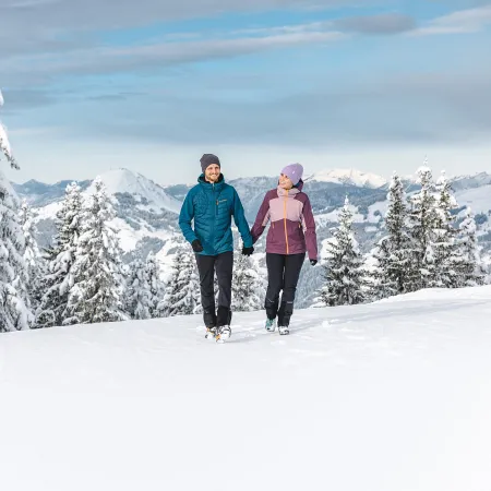 Zwei Frauen beim Winterwandern im Brixental, umgeben von verschneiten Bäumen.