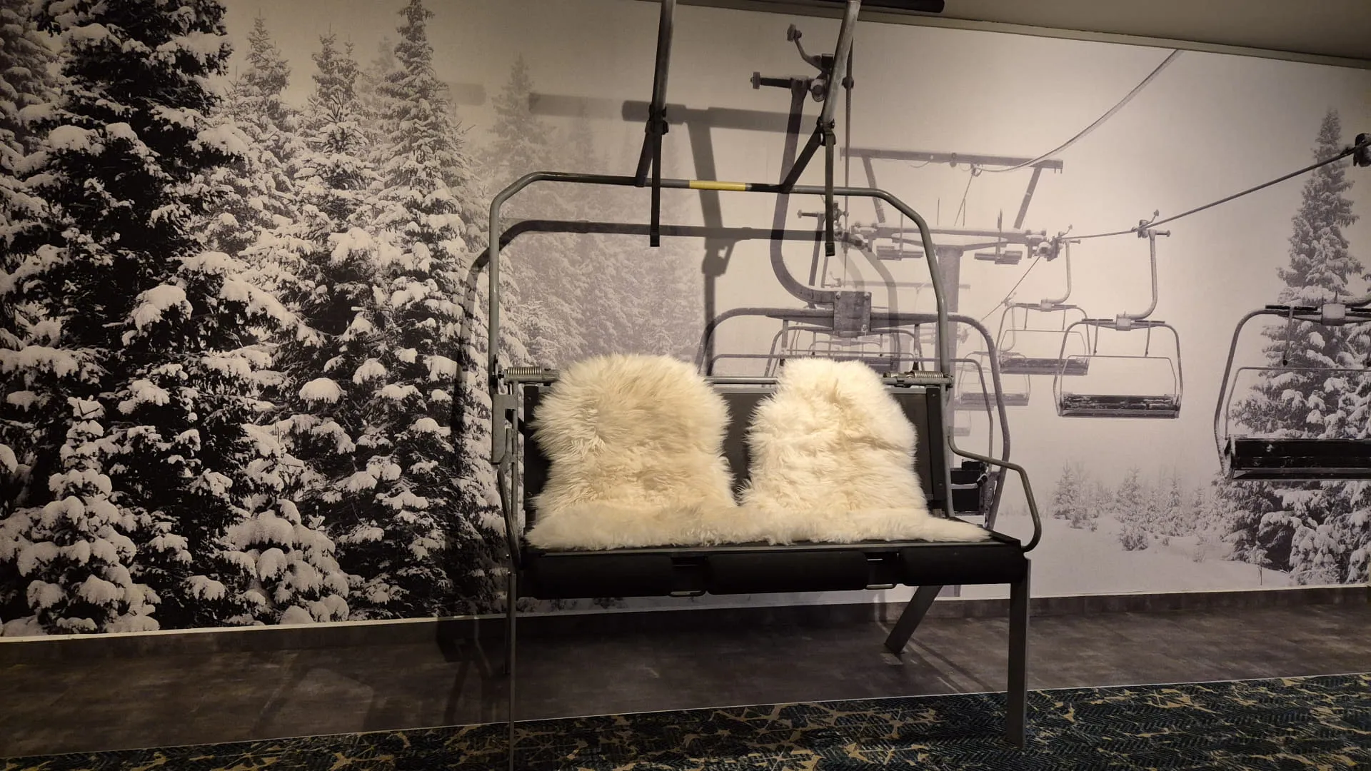 Skilift mit weißen Fellsitzbezügen vor einem schneebedeckten Wald