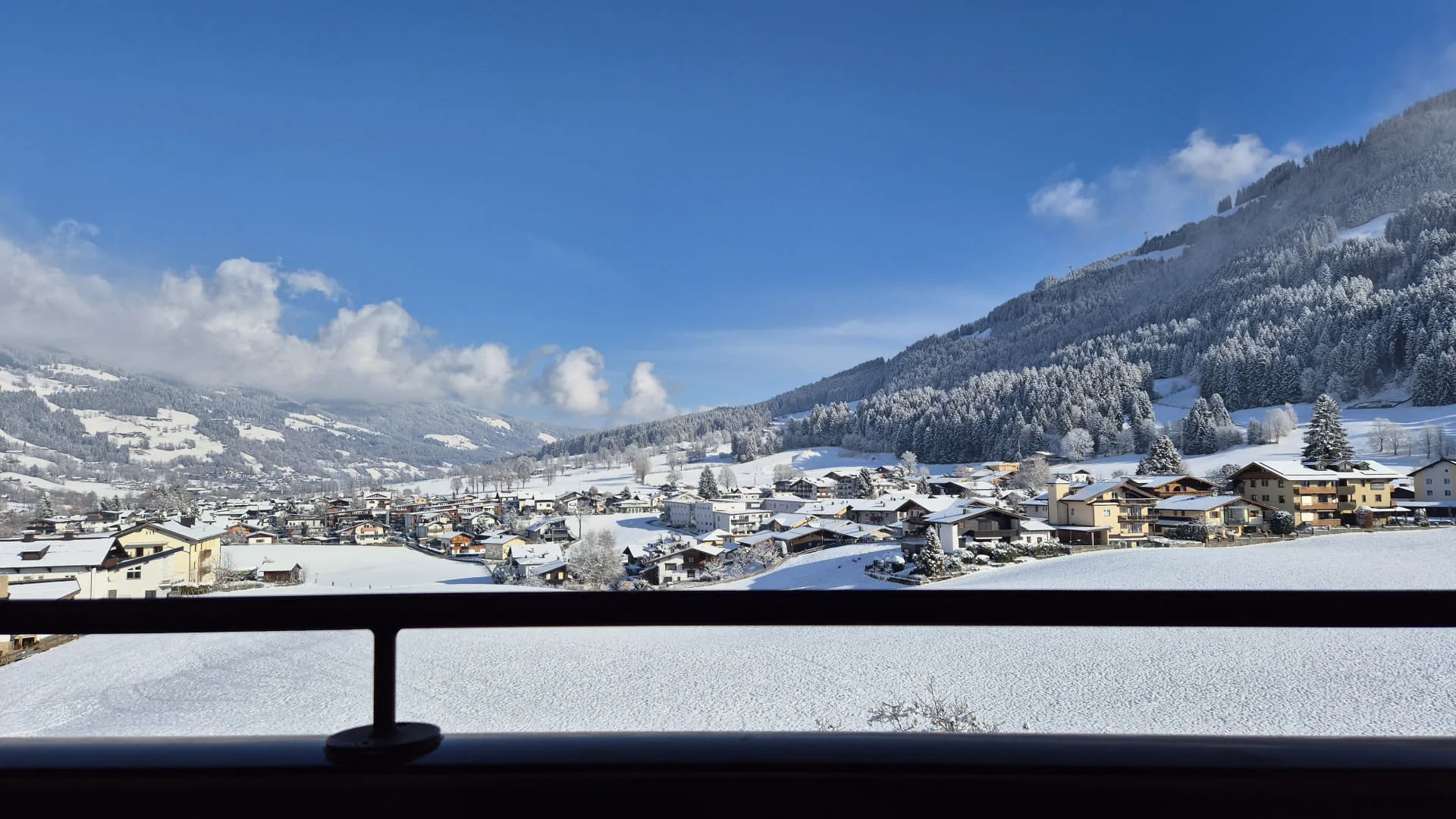 Blick auf ein verschneites Tal mit Häusern und Bergen im Hintergrund