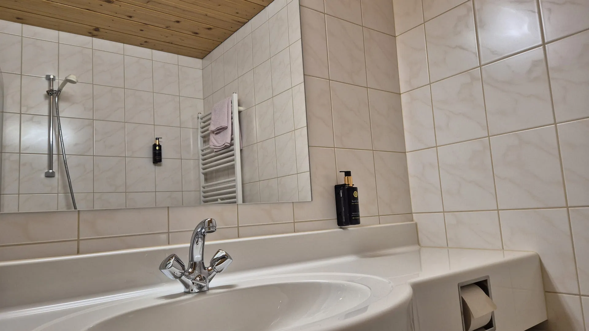 Waschbecken mit Wasserhahn und Spiegel, geflieste Wände, Holzdecke
